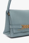 A close-up of a light blue Mini Chain Pouch Bag With Long Strap In Ice Leather with a structured design, gold-tone chain detail, and 'Victoria Beckham' embossed near the clasp.