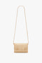 A small beige crossbody bag with a long strap and a gold chain detail on the front, reminiscent of a Mini Pouch With Long Strap In Sesame Leather by Victoria Beckham.