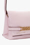 A close-up of a light pink Mini Chain Pouch Bag With Long Strap In Orchid Leather from Victoria Beckham featuring a gold chain detail and the brand name embossed on the lower front.