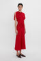 Woman in a Victoria Beckham Exclusive Gathered V-Neck Midi Dress In Carmine, standing against a white background.