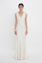 A person wearing a Gathered Shoulder Floor-Length Cami Gown In Ivory by Victoria Beckham stands against a plain white background.