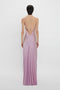 A woman with short, dark hair is wearing a backless, floor-length lilac satin slip dress with thin straps, reminiscent of Victoria Beckham's elegant designs. She is shown from the back in the Low Back Cami Floor-Length Dress In Rosa by Victoria Beckham.