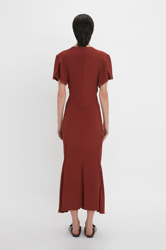 Back view of a person wearing a fitted, short-sleeve, Gathered V-Neck Midi Dress In Russet by Victoria Beckham with a zipper down the back made from figure-flattering stretch fabric, standing against a plain white background.