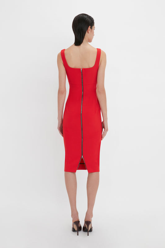 Back view of a person wearing a Victoria Beckham Sleeveless Fitted T-Shirt Dress In Bright Red made from stretch double wool crepe with a visible zipper running down the back, standing in black high heels against a plain white background.