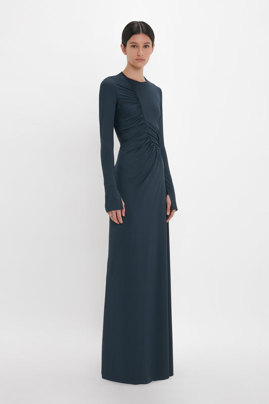 A person dons a Ruched Detail Floor-Length Gown In Midnight by Victoria Beckham, standing against a plain white background.