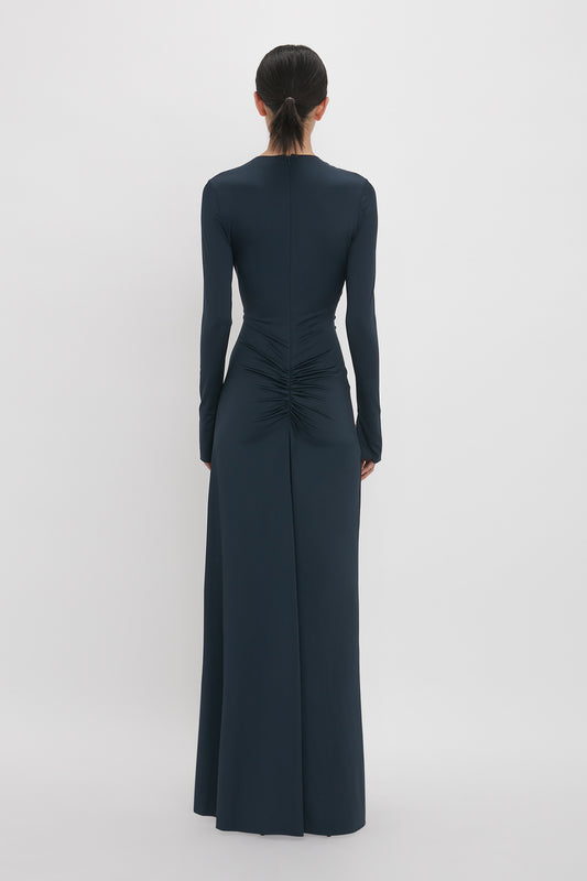 A person is shown from behind wearing a Victoria Beckham Ruched Detail Floor-Length Gown In Midnight.