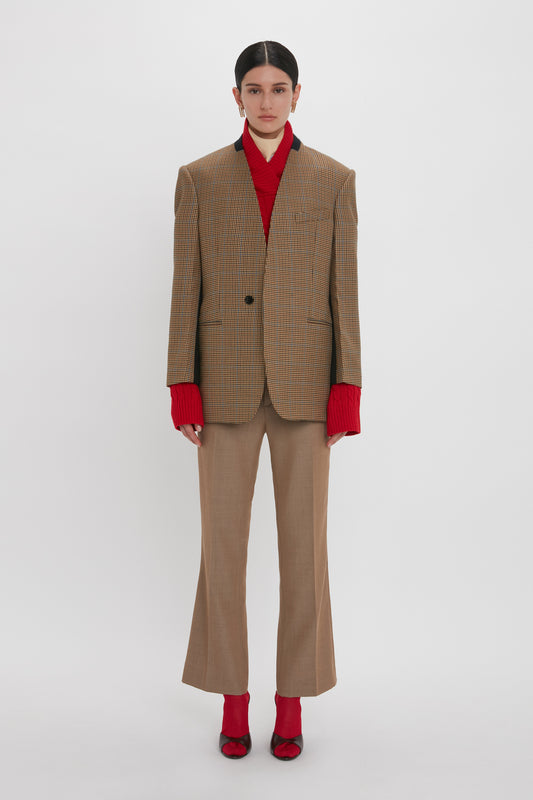 A person stands against a plain background wearing a Pocket Detail Collarless Jacket In Tobacco by Victoria Beckham, matching flared pants, and a red turtleneck sweater. They are also wearing red shoes.