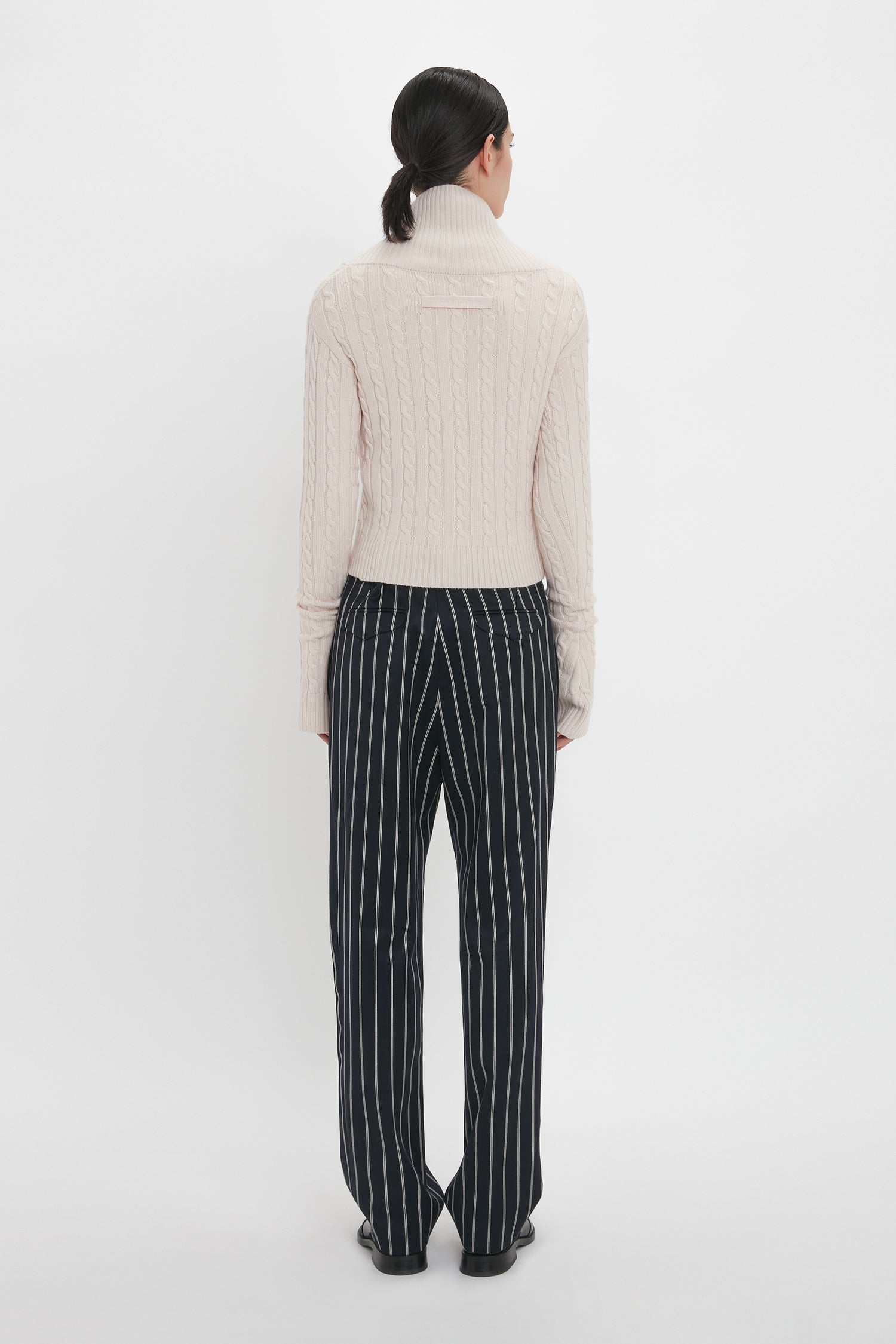 Person facing away, wearing a light-colored turtleneck sweater and Victoria Beckham Tapered Leg Trouser In Midnight-White.