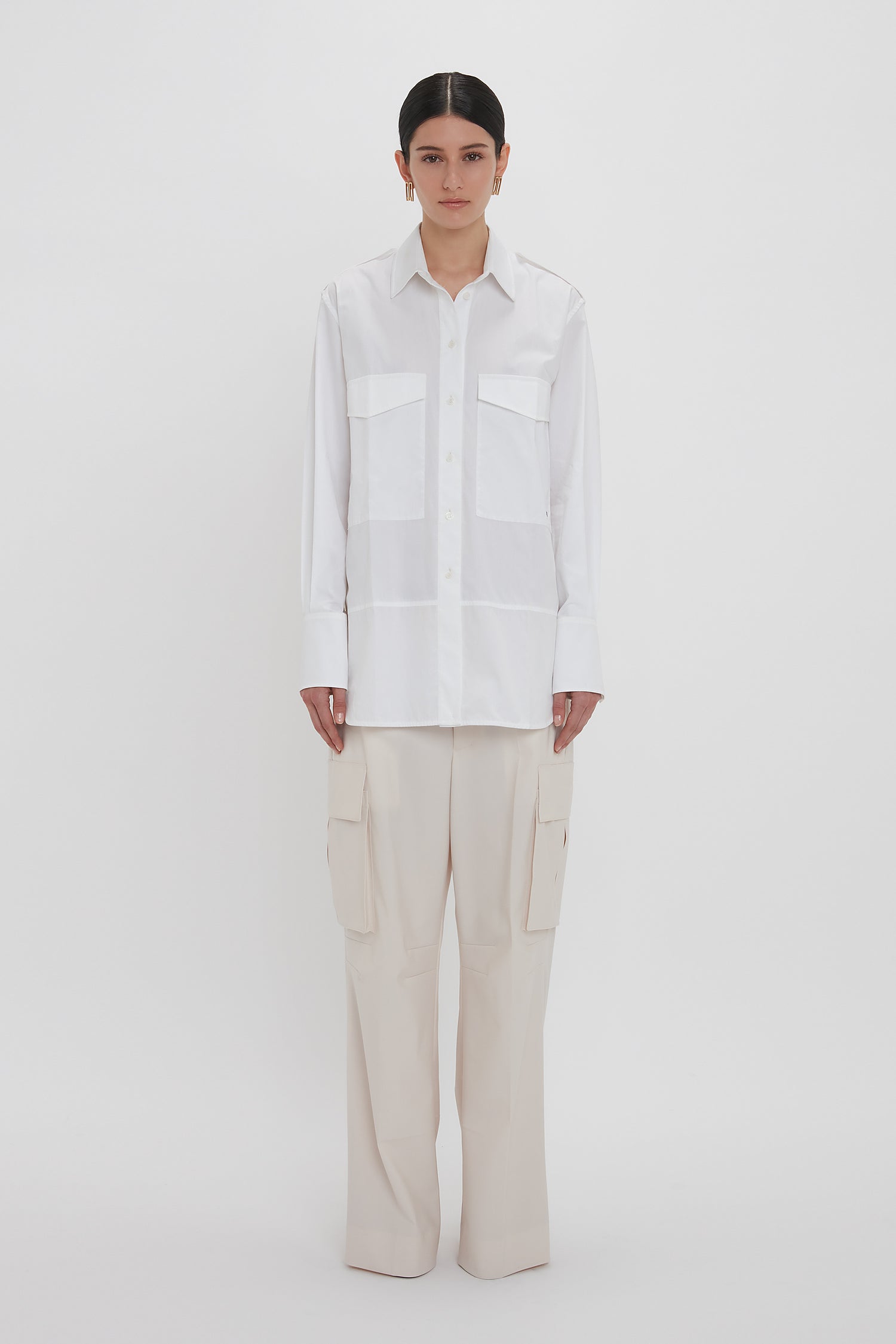 A person wearing an Oversized Pocket Shirt In White by Victoria Beckham made from organic cotton and beige cargo pants, standing against a plain white background.