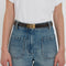 A person wearing blue denim jeans with large front pockets, a white t-shirt, and a Victoria Beckham Frame Belt In Espresso Croc Embossed Calf Leather with gold hardware on the buckle.