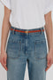 The person is wearing a white shirt tucked into high-waisted blue jeans with large front pockets and a versatile tan Exclusive Micro Frame Belt In Tan Leather by Victoria Beckham.