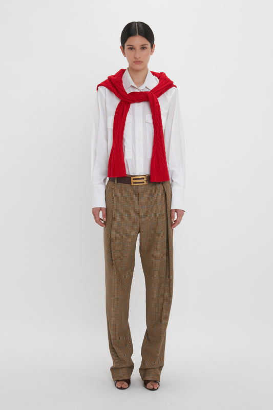 Person standing against a white background, wearing a white shirt, Asymmetric Chino Trouser In Tobacco/Multi by Victoria Beckham, a red sweater draped over their shoulders, and black shoes.
