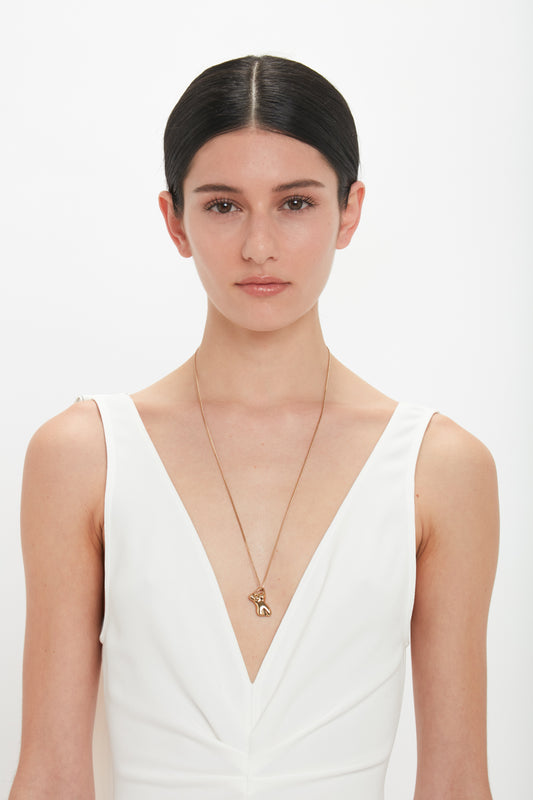 A person with straight dark hair, wearing a sleeveless white dress and an Exclusive Body Charm Necklace In Light Gold by Victoria Beckham made of 100% brass, stands against a plain white background.