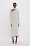 Person in a light-colored, Long Sleeve Cut-Out Jersey Midi Dress In Bone by Victoria Beckham with an asymmetrical hemline and split sleeves, standing against a plain white background.