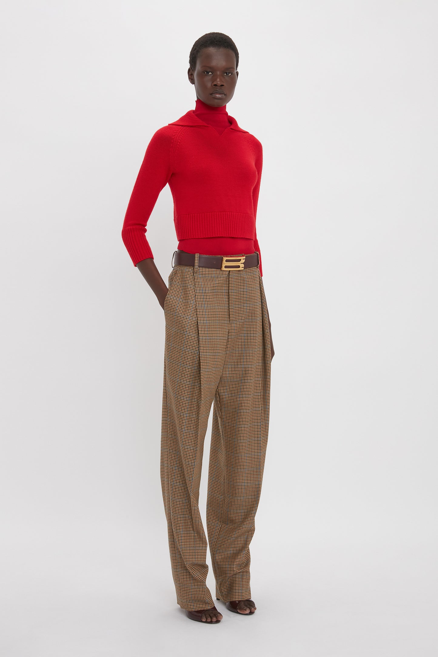 Person wearing a Victoria Beckham Double Layer Top In Deep Red, brown belt, and high-waisted plaid trousers, standing against a plain white background.