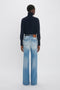 Rear view of a person wearing a dark turtleneck sweater and Victoria Beckham Alina High Waisted Jean In Light Summer Wash against a plain white background.