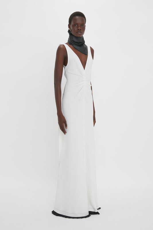 A person wearing a sleeveless, white, Exclusive V-Neck Gathered Waist Floor-Length Gown In Ivory by Victoria Beckham and a black scarf poses against a plain white background.
