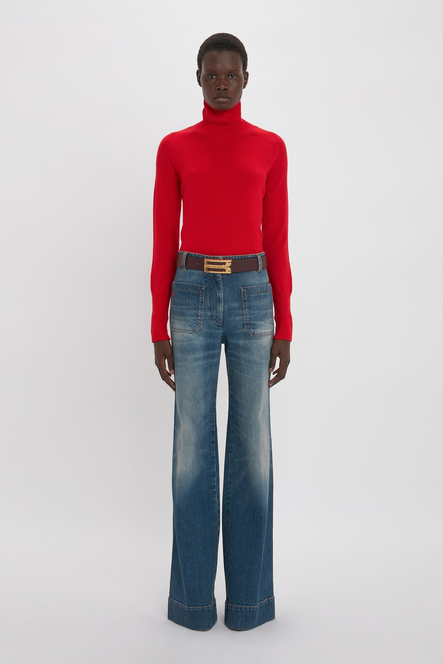 Person wearing a red Victoria Beckham Polo Neck Jumper In Red and wide-leg blue jeans standing against a plain white background.