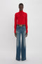 Person wearing a red Victoria Beckham Polo Neck Jumper In Red and wide-leg blue jeans standing against a plain white background.