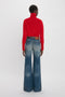 Person facing away, wearing a Victoria Beckham red turtleneck sweater and Alina High Waisted Jean In Heavy Vintage Indigo Wash.