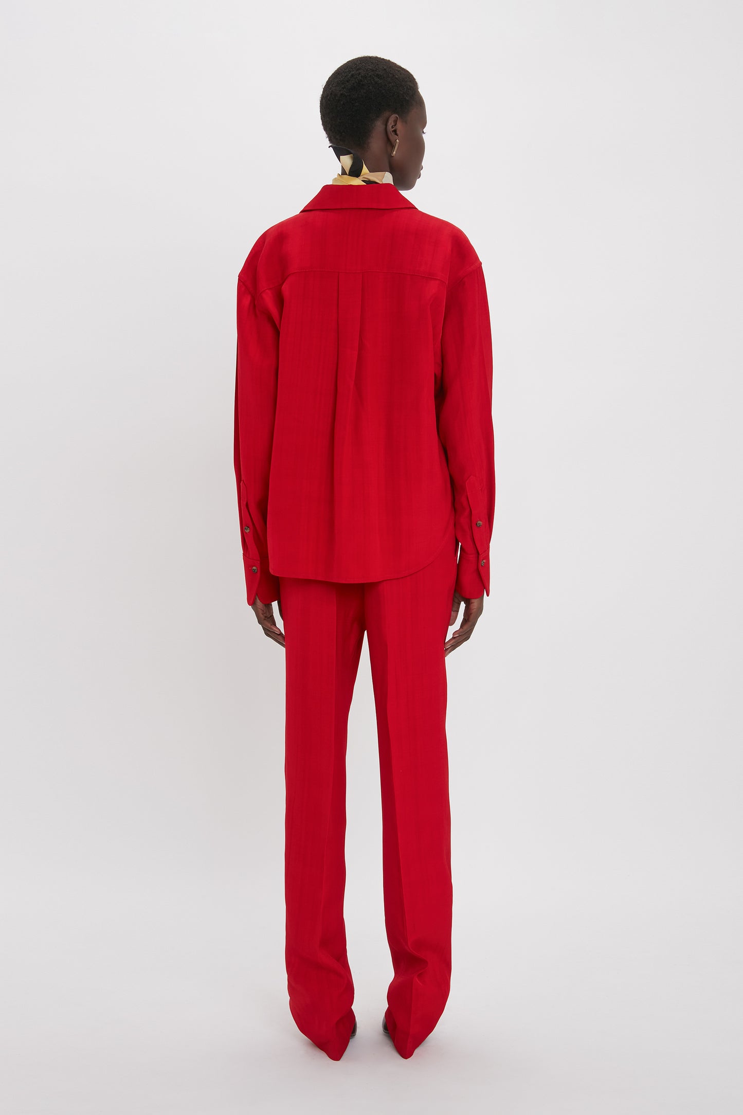 Person standing against a white background, wearing a masculine-inspired red Cropped Long Sleeve Shirt In Carmine by Victoria Beckham and matching pants, viewed from the back.