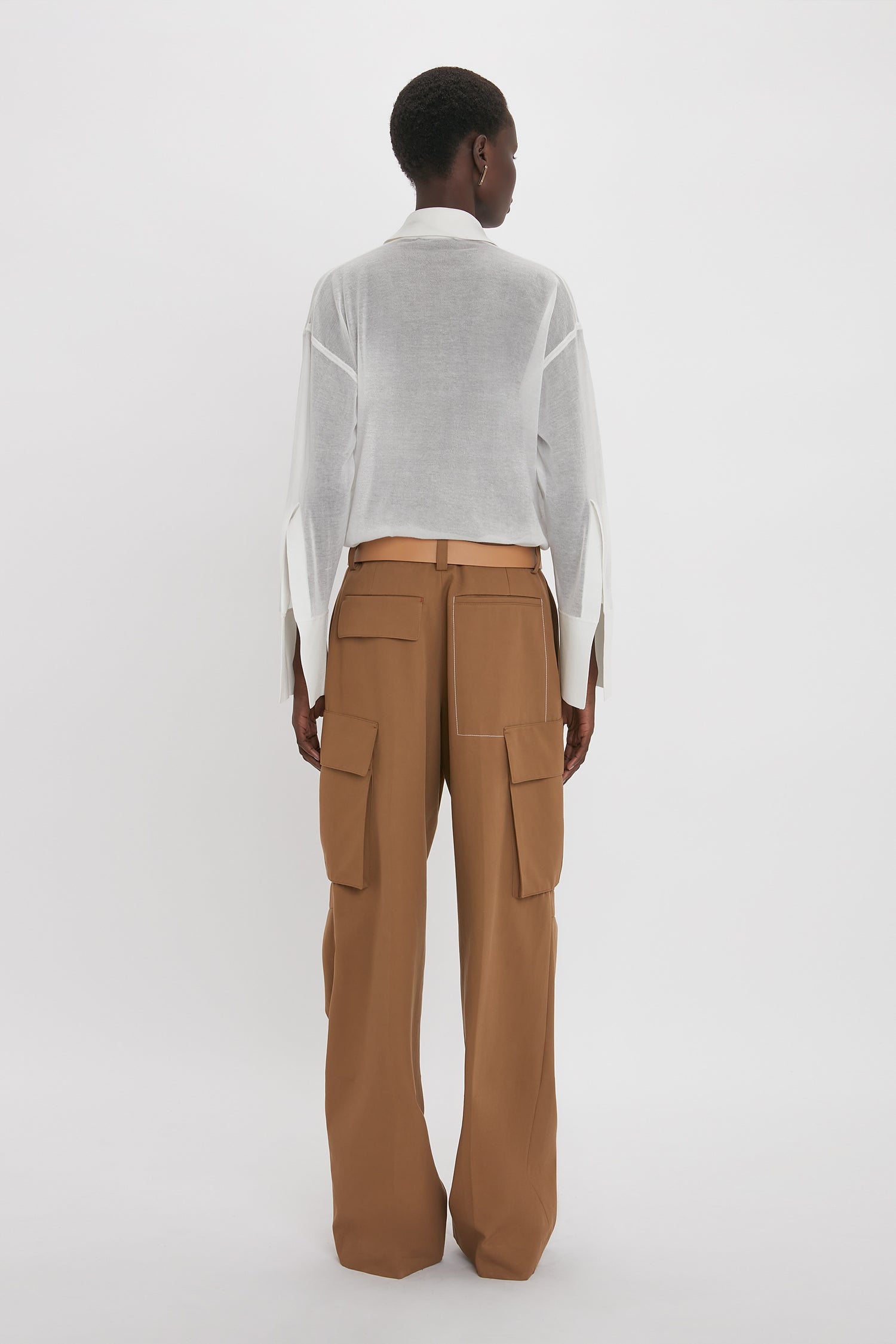 Person wearing a white semi-sheer Pocket Detail Shirt In White by Victoria Beckham and brown high-waisted cargo pants with a relaxed fit, shown from the back, against a plain white background.