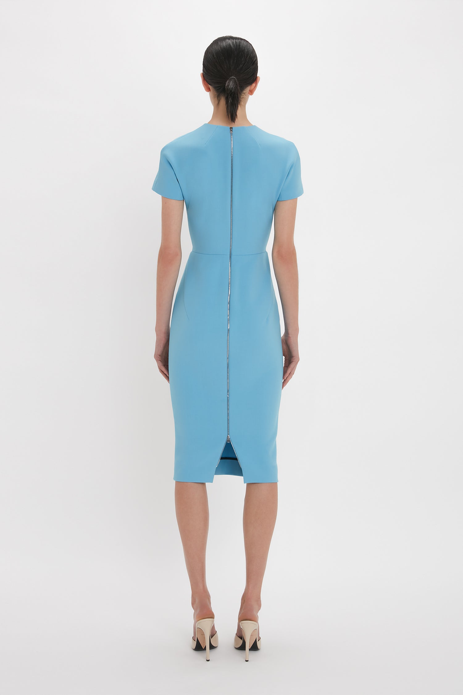 Rear view of a person wearing a Victoria Beckham Exclusive Fitted T-Shirt Dress in periwinkle blue, with a visible back zipper, standing against a plain white background.