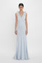 A person stands facing forward, wearing an Exclusive Gathered Shoulder Cami Floor-Length Gown In Ice Blue by Victoria Beckham made of luxurious crepe back satin with a deep V-neckline, against a plain white background.