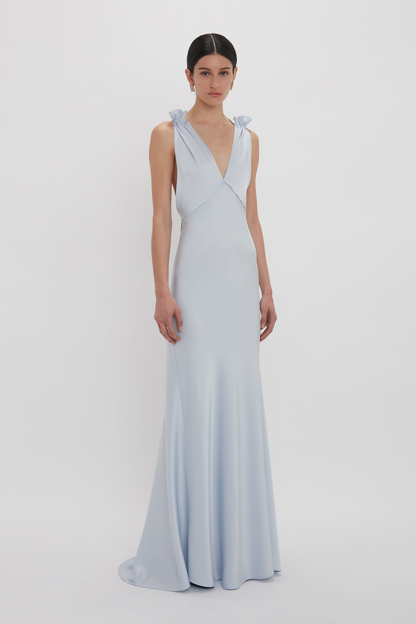 A woman stands against a plain white background wearing a floor-length Exclusive Gathered Shoulder Cami Floor-Length Gown In Ice Blue by Victoria Beckham, made of luxurious crepe back satin.