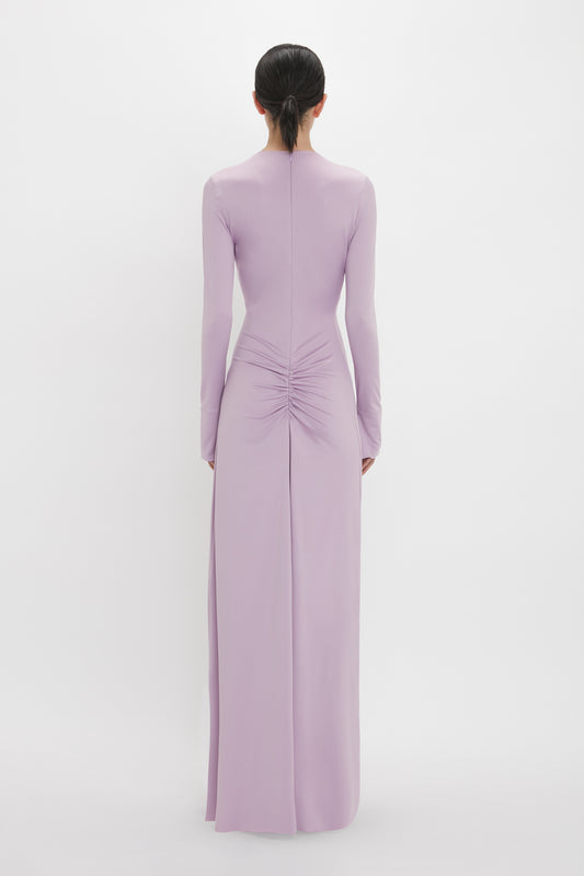 Person wearing a long-sleeved, Ruched Detail Floor-Length Gown In Petunia by Victoria Beckham with a ruched detail at the lower back, standing with their back to the camera against a plain white background.
