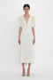 Person wearing a Victoria Beckham Exclusive V-Neck Ruffle Midi Dress In Ivory with puffed short sleeves and open-toe shoes, standing against a plain white background.