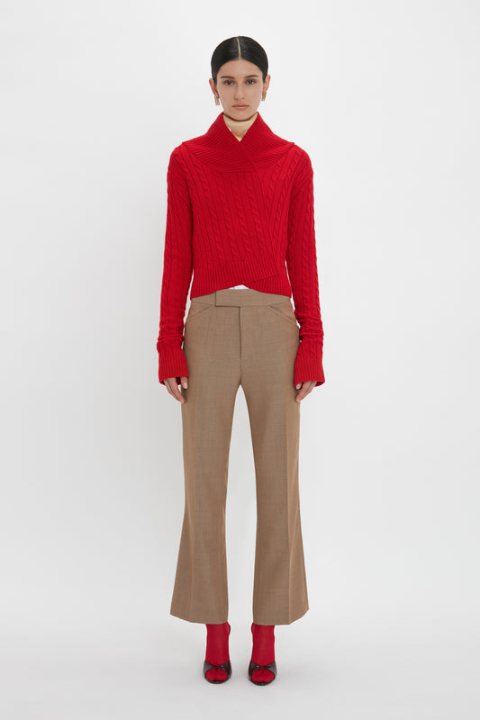 Person wearing a red knit sweater, Victoria Beckham's Wide Cropped Flare Trouser In Tobacco, and red high-heeled shoes stands against a plain white background.