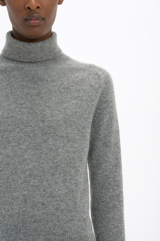 A person wearing a Victoria Beckham Polo Neck Jumper In Grey Melange stands against a white background. Only the lower half of the face and upper torso are visible, highlighting the garment's versatile styling options.
