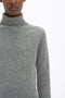 A person wearing a Victoria Beckham Polo Neck Jumper In Grey Melange stands against a white background. Only the lower half of the face and upper torso are visible, highlighting the garment's versatile styling options.