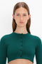 A person with long brown hair wears a VB Body Cropped Cardi In Lurex Green by Victoria Beckham, showcasing a form-fitting silhouette. Facing the camera with a neutral expression against a white background, the look exudes feminine sensibility.