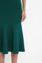 A person wearing a Victoria Beckham VB Body Flared Skirt In Lurex Green, shown from the waist down with one arm visible.