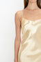 A woman wearing an Exclusive Floor-Length Cami Dress In Gold by Victoria Beckham stands against a plain white background, evoking a 1990s-inspired elegance.