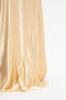 Close-up of a floor-length, shiny golden fabric with a smooth texture, draped in soft folds, reminiscent of Victoria Beckham's Exclusive Floor-Length Cami Dress In Gold.