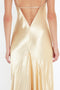 Back view of a person wearing the Victoria Beckham Exclusive Floor-Length Cami Dress In Gold with thin straps and a deep V-shaped back, reminiscent of 1990s-inspired fashion.