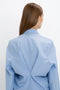 A person with long, straight brown hair facing away, wearing a light blue collared Pleat Detail Raglan Shirt In Oxford Blue by Victoria Beckham with a concealed button-front closure and a prominent back detail.