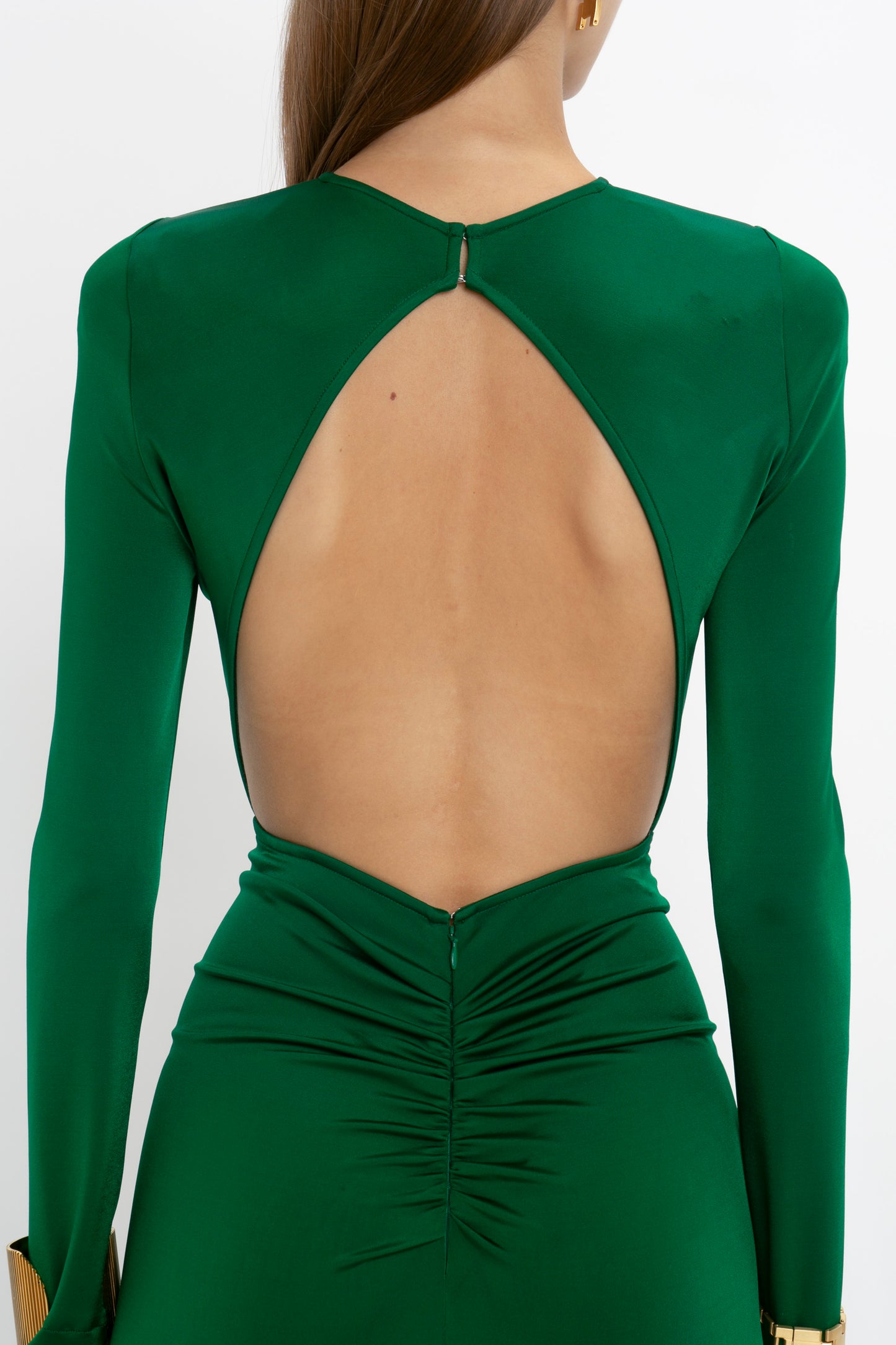 A person wearing the Circle Detail Open Back Gown In Emerald by Victoria Beckham, featuring a large open back and ruched detailing at the lower back, resembling an elegant exposed back gown.