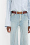 Person wearing a blue and white striped shirt tucked into light blue denim Bianca Jean In Light Blue Denim by Victoria Beckham with a brown belt featuring a gold buckle.