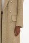 Close-up of a person wearing a textured, buttoned beige blazer with a pocket. Their left hand is partially visible, resting beside their body, showcasing the relaxed modern fit reminiscent of Victoria Beckham's Exclusive Waisted Tailored Coat In Flax.