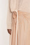 Close-up of a person wearing a Victoria Beckham Wrap Front Cardigan In Nougat and a matching shimmering peach skirt with fabric rose and draped details, evoking the stylish elegance of Victoria Beckham.