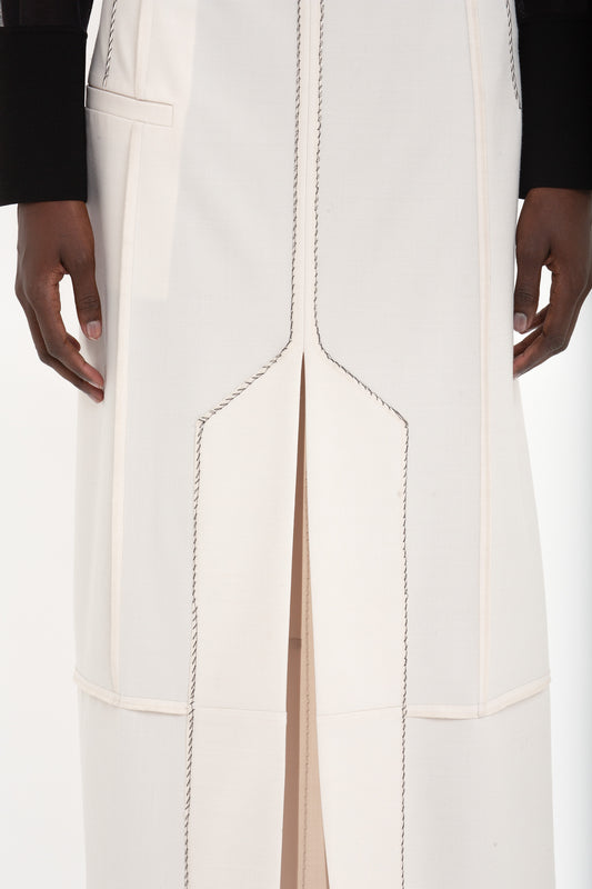 Close-up of a person wearing the Deconstructed Floor-Length Skirt In Bone by Victoria Beckham, featuring black stitching details, exposed seams, and a front slit, standing against a plain background. Only the lower torso and hands are visible.