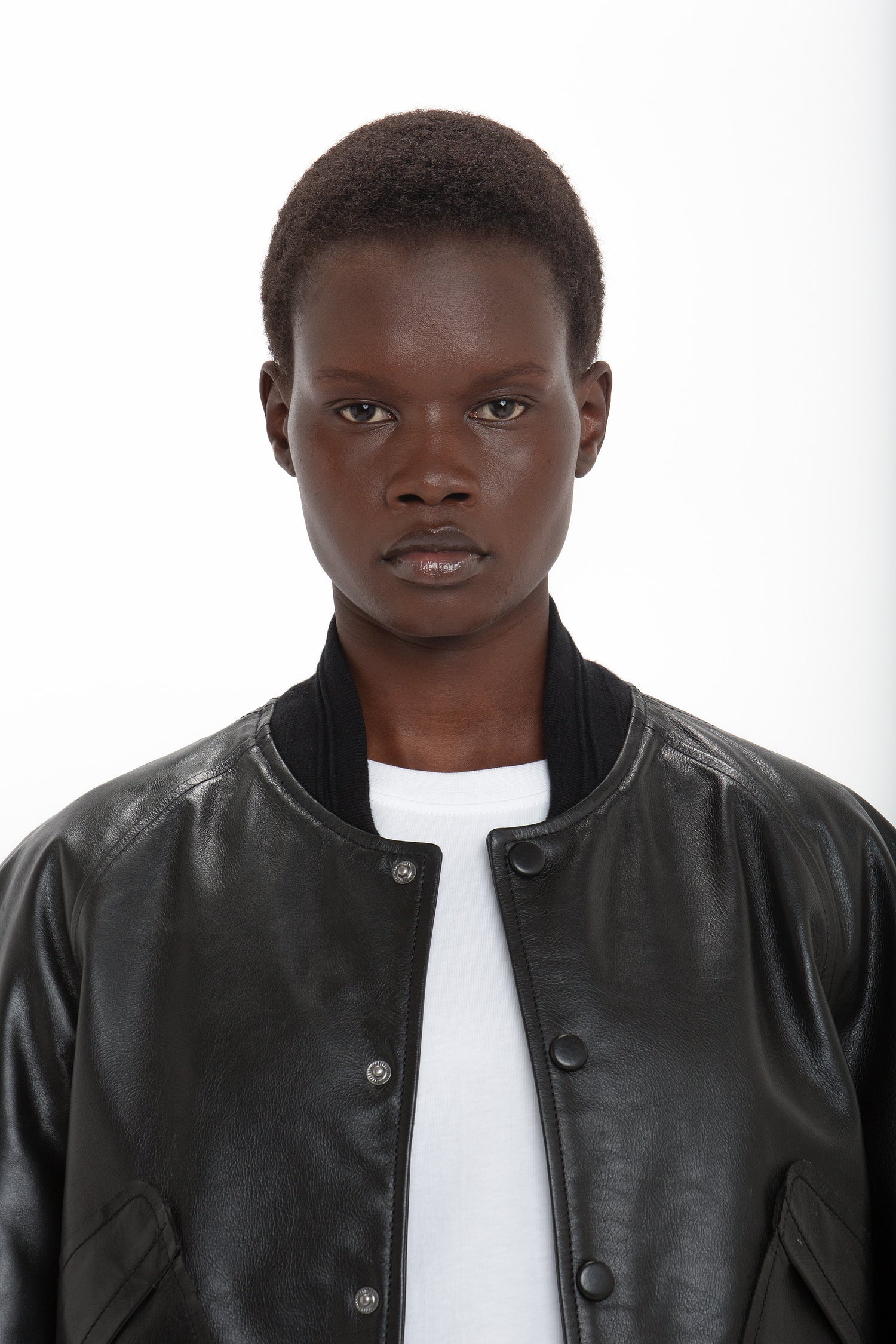 Person wearing a white shirt and a Victoria Beckham Leather Varsity Jacket In Black, looking directly at the camera on a plain white background.