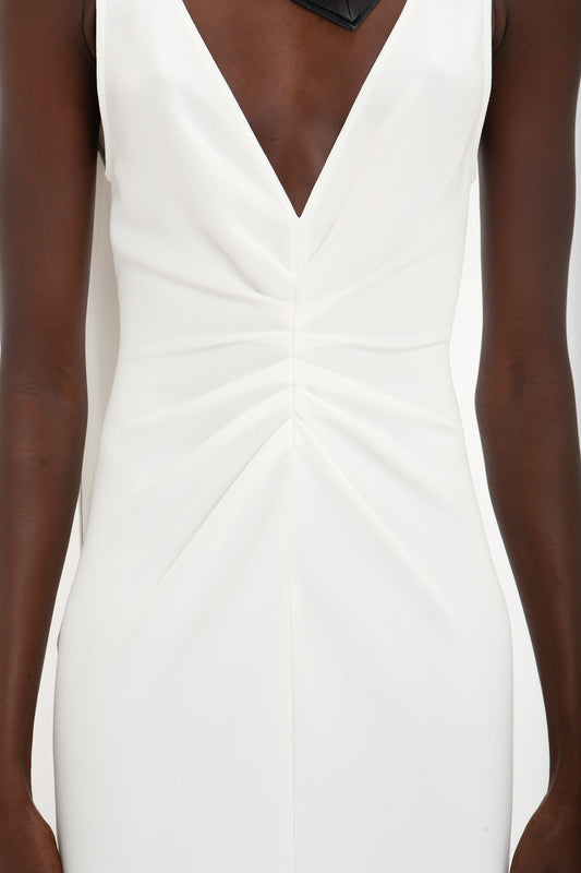 A close-up of a woman wearing an Exclusive V-Neck Gathered Waist Floor-Length Gown In Ivory from the Victoria Beckham brand, featuring a sleeveless white design with a deep V-neckline and gathered detailing at the front.