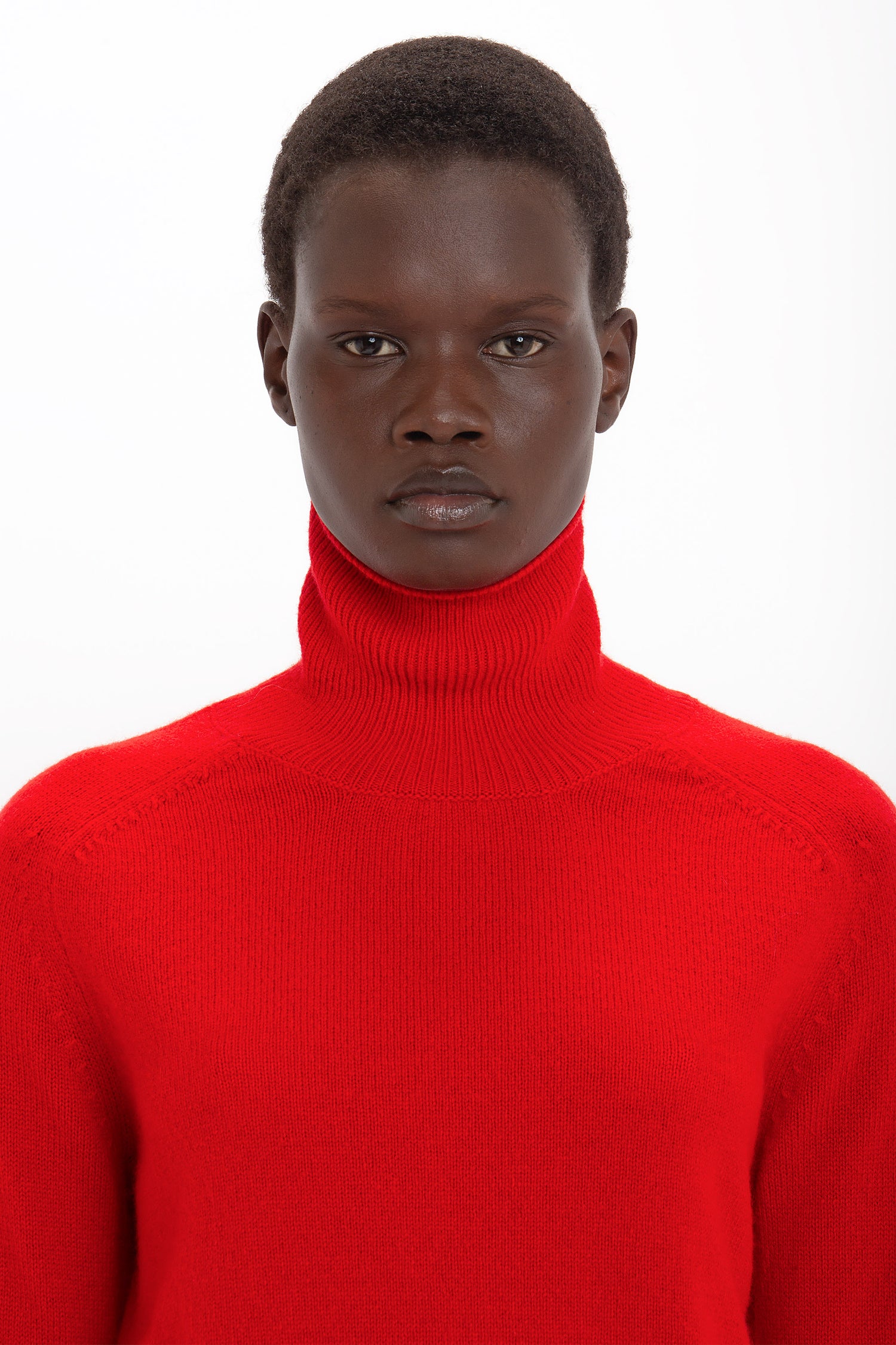 A person with short hair is wearing a bright red Victoria Beckham Polo Neck Jumper In Red and looking directly at the camera.