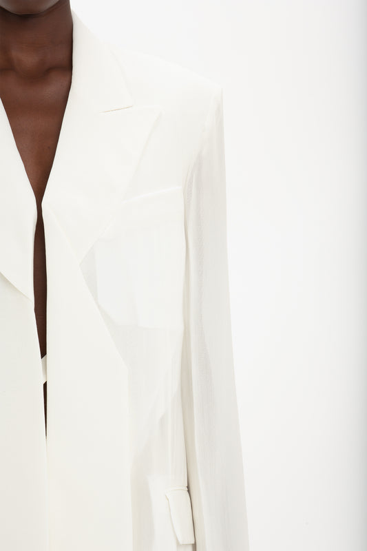 Cropped view of a person wearing a Fold Detail Tailored Jacket In White by Victoria Beckham, showcasing the upper part of the tailored jacket, focusing on the lapel, pocket, and shoulder area against a plain background.