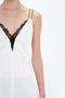 Close-up of a person wearing an ivory sleeveless dress with a plunging neckline edged in black lace, reminiscent of the Lace Detail Cami Top In Harvest Ivory by Victoria Beckham.